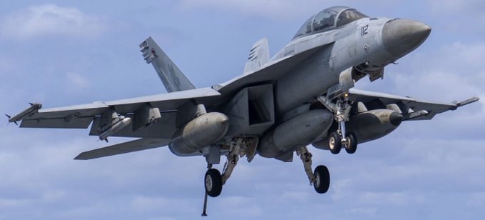 First image displays a gray F/A-18F Super Hornet fighter jet in flight over water with landing gear extended and wings folded slightly, viewed from the side against a blue sky. Second image shows a gray MH-60R Sea Hawk helicopter hovering low with rotors spinning, open side door revealing interior, and landing gear visible, set against a cloudy sky.