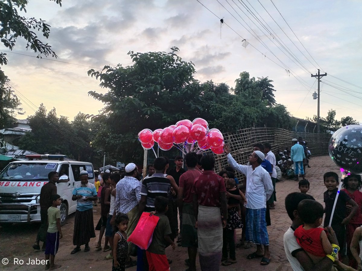 A #Rohingya man sells colourful balloons inside Cox’s Bazar #refugee camp, as people of all ages gather around with smiles and hopeful faces. Amid hardship and uncertainty, moments like this remind us that the human spirit still finds reasons to smile.🎈🎈

#Humanity
#RefugeeCamp
