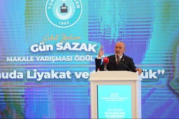 First image shows a man in a dark suit speaking at a podium with a microphone, gesturing with his hand raised, against a blue backdrop featuring the text Gün Sazak Makale Yarışması Ödül Töreni and a 1992 emblem. Second image depicts a group of about 15 people in formal suits and one woman in professional attire standing together on a stage with Turkish flags, red and blue banners, and a logo possibly for MHP. Third image captures a bald man in glasses and a dark suit holding a microphone at a white podium, gesturing openly, with a large projected image of another man behind him and wooden paneling in the background. Fourth image features two men in suits, one with a mustache receiving a red plaque award from the other, standing before a purple and blue backdrop with Turkish flags and text for Sabiha Gökçen Gün Sazak Liyakat ve Dürüstlük Makale Yarışması.