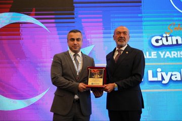 First image shows a man in a dark suit speaking at a podium with a microphone, gesturing with his hand raised, against a blue backdrop featuring the text Gün Sazak Makale Yarışması Ödül Töreni and a 1992 emblem. Second image depicts a group of about 15 people in formal suits and one woman in professional attire standing together on a stage with Turkish flags, red and blue banners, and a logo possibly for MHP. Third image captures a bald man in glasses and a dark suit holding a microphone at a white podium, gesturing openly, with a large projected image of another man behind him and wooden paneling in the background. Fourth image features two men in suits, one with a mustache receiving a red plaque award from the other, standing before a purple and blue backdrop with Turkish flags and text for Sabiha Gökçen Gün Sazak Liyakat ve Dürüstlük Makale Yarışması.