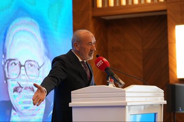 First image shows a man in a dark suit speaking at a podium with a microphone, gesturing with his hand raised, against a blue backdrop featuring the text Gün Sazak Makale Yarışması Ödül Töreni and a 1992 emblem. Second image depicts a group of about 15 people in formal suits and one woman in professional attire standing together on a stage with Turkish flags, red and blue banners, and a logo possibly for MHP. Third image captures a bald man in glasses and a dark suit holding a microphone at a white podium, gesturing openly, with a large projected image of another man behind him and wooden paneling in the background. Fourth image features two men in suits, one with a mustache receiving a red plaque award from the other, standing before a purple and blue backdrop with Turkish flags and text for Sabiha Gökçen Gün Sazak Liyakat ve Dürüstlük Makale Yarışması.