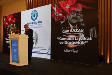 First image shows a man in a suit speaking at a podium with a microphone in front of a blue backdrop featuring the Gün Sazak name and themes of merit and honesty in public service, alongside a large portrait of Gün Sazak wearing glasses and a mustache. Second image depicts a man in a suit holding a microphone at a podium with a wooden backdrop and a large black-and-white portrait of Gün Sazak, text reading Gün Sazak Makale Yarışması and Kamuda Liyakat ve Dürüstlük. Third image displays a man in a suit speaking at a podium with a microphone, blue backdrop with Türk Büro-Sen logo and Gün Sazak portrait, text on merit and honesty in public service. Fourth image features a group of about 15 people in formal suits and dresses standing on a stage with a blue backdrop displaying a circular emblem.