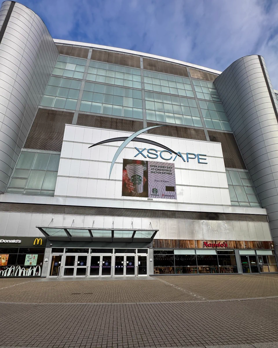 Exterior view of the Xscape entertainment complex, featuring a modern architectural design with prominent branding, alongside storefronts of McDonald's and Nando's at street level.