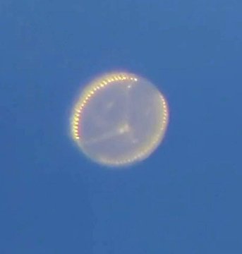 First image displays a glowing circular object with a translucent white interior and subtle internal cross-like structure outlined by a bright yellowish rim against a clear blue sky. Second image shows a bright white streak resembling a light trail or object moving across the blue sky with green leafy foliage visible in the lower right corner.