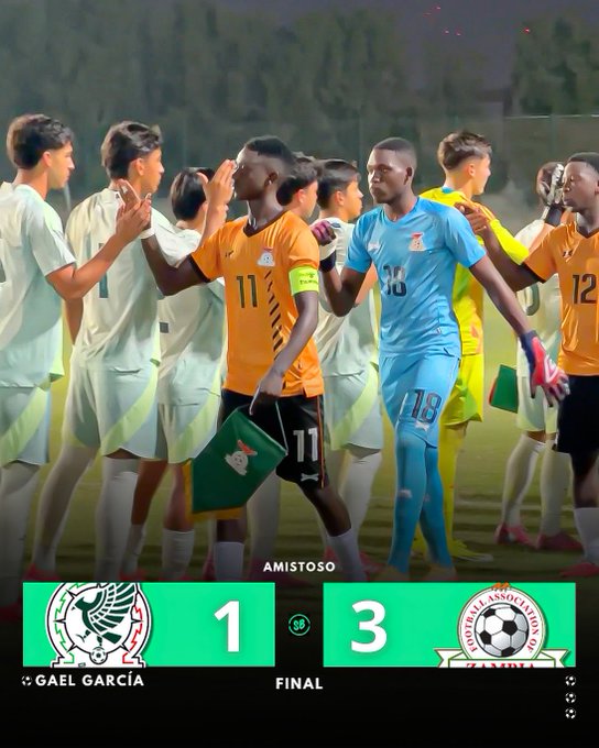 Scoreboard shows Mexico 1 - 3 Zambia in final of friendly match. Gael Garcia listed as scorer. Players from both teams in green Mexico and orange Zambia uniforms stand grouped together clapping and holding flags post-game. Bottom features Mexico and Zambia association logos.