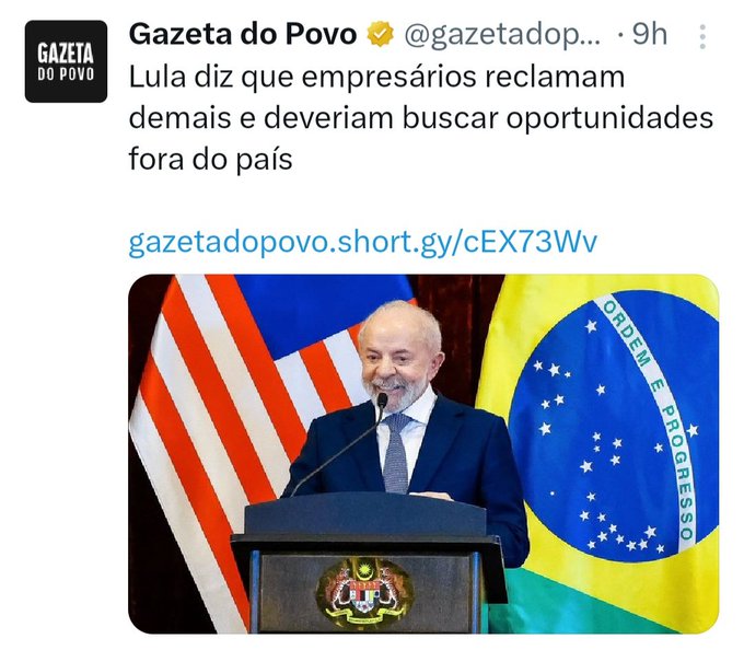 A man in a suit and tie stands at a wooden podium with microphones, smiling slightly while speaking. Brazilian and United States flags are positioned behind him on either side. The GazetadoPovo logo and article headline in Portuguese about Lula criticizing complaining entrepreneurs appear overlaid on the image.