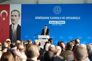 First image shows a man in suit kneeling and hugging two young girls in school uniforms with backpacks, one wearing a red hooded cape and headband with crescent moon, smiling together outdoors with other suited men in background. Second image depicts a man in suit speaking at a podium on a stage with blue backdrop featuring Turkish flags, Atatürk portrait, and text Gümüşdere İlkokulu ve Ortaokulu Açılış Töreni, audience seated in front. Third image captures a large group of adults and children in formal attire cutting a ribbon under balloon arch with Gümüşdere Okulu sign at building entrance. Fourth image shows diverse group of suited men and women, some with headscarves, seated around a wooden table in a library with bookshelves, Turkish flags, childrens drawings on wall, and vase of flowers.