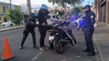 Multiple images show uniformed police officers from PNC de Guatemala conducting identifications on streets in Colonia Bethania. Officers in black tactical gear and helmets interact with civilians wearing hoodies and helmets near black and blue motorcycles with license plates. Traffic cones are placed around the scene, with parked cars, trees, and colorful buildings in the background. One image captures an officer holding a persons arm while another stands nearby with a motorcycle. Another shows officers surrounding a motorcycle with a rider removing a helmet. Additional views depict group interactions with vehicles and pedestrians present.