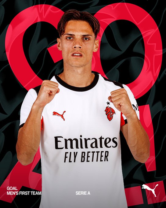 A young male athlete with short dark hair and focused expression stands in a celebratory pose with arms raised and fists clenched, wearing a white short-sleeved soccer jersey with black trim, red accents, a red devil emblem on the chest, Puma logo on the sleeve, and Emirates Fly Better sponsor text across the front, set against a graphic background with red heart shapes and the number 1 in large red font, with text overlays reading Mens First Team Serie A and Puma at the bottom.