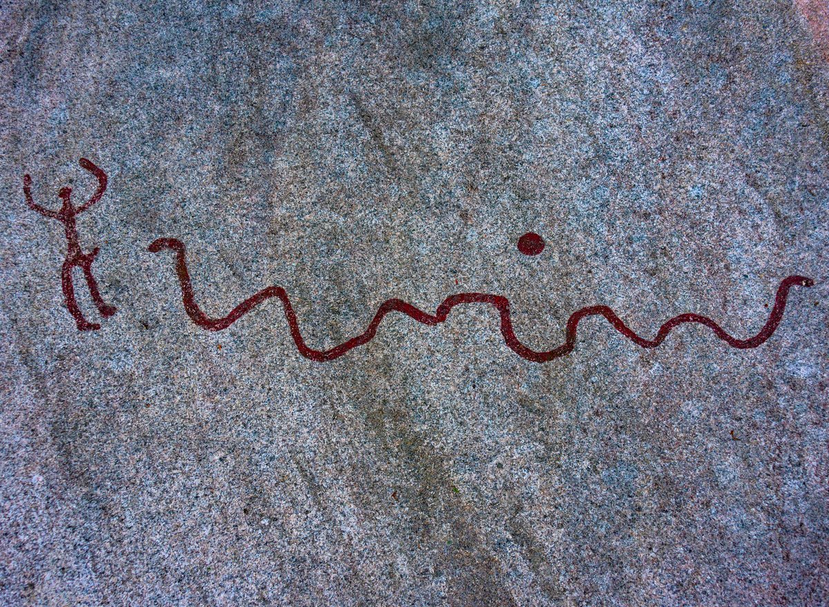 Bronze Age rock carving with a raised‑armed human, a serpent‑like wavy line and a single cup‑mark. Site: Tanum World Heritage, Vitlycke area, Bohuslän, Sweden. Date: c. 1700–500 BC. Medium: petroglyph pecked into granite, with modern red pigment added for visibility.