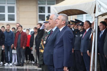 First image shows a group of people including suited officials and children gathered outside a building with Turkish flags, palm trees, and a police vehicle nearby. Second image depicts officials in suits and military uniforms standing under white tents with emblems, surrounded by attendees. Third image captures individuals holding flags in blue and red, with children and adults in casual and formal attire near a building facade. Fourth image features military personnel and officials saluting or standing formally outside a beige building with a tent.