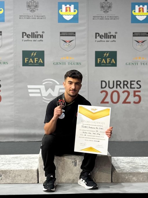 Young male athlete in black tracksuit and sneakers stands on podium holding gold medal around neck and certificate in hand with Turkish flag colors visible on backdrop. Backdrop features European Weightlifting Federation logos sponsors like Pellini coffee and event details for Durrës 2025. Another image shows group of athletes and officials on podium with medals including gold silver bronze recipients in athletic wear some in traditional Albanian attire posing together. Third image depicts same athlete seated on podium edge holding silver medal and certificate with similar backdrop elements including flags and sponsor banners.