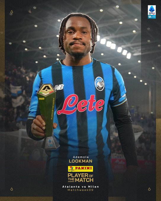 Ademola Lookman stands on a soccer field under stadium lights, wearing a blue and black Atalanta jersey with New Balance and Lotto logos, holding a green trophy labeled A with gold accents, smiling confidently, with Panini branding and text below identifying him as Player of the Match for Atalanta vs Milan.
