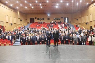 First image shows a large auditorium filled with seated audience members in formal attire including suits and ties, viewed from the stage with red chairs and wooden paneling. Second image depicts a man in a dark suit with tie speaking into a microphone on stage, standing near banners for educational organizations and a screen. Third image captures the auditorium with audience seated and a man in suit speaking on stage from a side angle. Fourth image features two men in suits holding a green ornate plaque on stage, with a projection screen displaying event title Türkiye Yüzyılı Maarif Modeli and names Prof. Dr. Cihad Demirli and others.