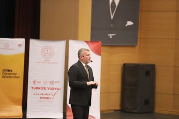 First image shows a large auditorium filled with seated audience members in formal attire including suits and ties, viewed from the stage with red chairs and wooden paneling. Second image depicts a man in a dark suit with tie speaking into a microphone on stage, standing near banners for educational organizations and a screen. Third image captures the auditorium with audience seated and a man in suit speaking on stage from a side angle. Fourth image features two men in suits holding a green ornate plaque on stage, with a projection screen displaying event title Türkiye Yüzyılı Maarif Modeli and names Prof. Dr. Cihad Demirli and others.