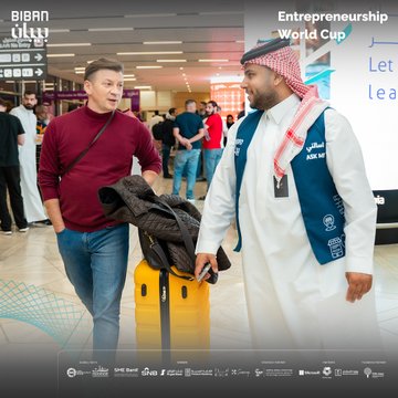 First image shows two men in Biban entrepreneurship vests, one wearing a blue cap and black jacket holding a black suitcase, the other in white thobe and red headscarf standing near UN Tourism and Qatar Airways banners in an airport terminal with other travelers and luggage. Second image depicts a man in red headscarf and blue vest conversing with a woman in black top and colorful skirt carrying a beige bag, near airport signage and other passengers. Third image features a man in glasses and black shirt holding a Texas flag next to a man in blue vest and white thobe carrying a yellow suitcase, with airport displays and diverse individuals in background. Fourth image captures a man in maroon sweater holding a yellow suitcase talking to a man in red headscarf and blue vest, surrounded by men in various attire near flight information screens in a modern airport setting. All images include Biban forum logos, World Cup for Entrepreneurship text in Arabic and English, and sponsor mentions like SME Bank.