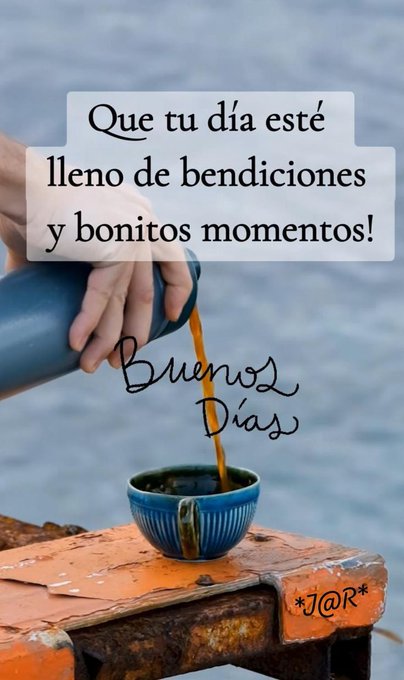 A hand holds a blue thermos pouring hot coffee into a blue ceramic mug placed on an orange wooden surface. Text overlays in white and yellow read Que tu dia este lleno de bendiciones y bonitos momentos at the top and Buenos dias at the bottom. The background features a blurred blue sky and water. A small JQ R watermark appears on the wooden surface.