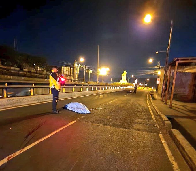 First image shows a nighttime road scene on Carretera al AtlÃ¡ntico with a person in a yellow safety vest standing near a blue tarp-covered body on the asphalt beside a bridge railing and streetlights. Second image depicts a nighttime street with pink buildings a fallen motorcycle with visible front damage lying on its side near police lights and a yellow barrier.