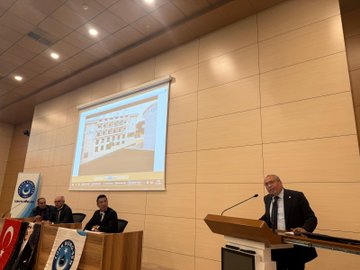 First image shows a man in a dark suit and tie standing at a wooden podium with microphones, gesturing with both hands outstretched, in front of a light wooden wall and two Turkish flags on poles. Second image depicts a conference room with a projection screen displaying a title FARKLILIK CUNKU and images of documents and a logo, three men in suits seated at a table with microphones, Turkish flags and banners for Turk Buro-Sen and Turkiye Kamu-Sen on the table and walls, a large portrait of Mustafa Kemal Ataturk. Third image features a modern building projected on a screen behind a podium, several men in suits seated and one speaking at the podium with a microphone, banners with eye symbols and Turkish flags on wooden tables. Fourth image shows a large group of about 30 people mostly men in suits standing in rows on a stage with blue backdrop, some holding documents, in a formal assembly setting.