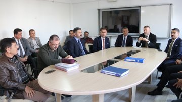 First image shows a group of adults seated in a modern room with white walls, plants, and educational posters, some wearing suits and headscarves, engaged in discussion around low tables with notebooks and bags. Second image depicts men in formal suits and jackets sitting around an oval wooden table with documents and a phone, one man gesturing while speaking. Third image captures a seminar in a wood-paneled auditorium with red seats, a screen displaying Turkish flag and text, speakers at a podium, and audience members including women in headscarves listening attentively. Fourth image features a group of about ten adults, men in suits and women in headscarves and coats, standing in a line in front of a stone building with arched windows and a sign reading 1864 above the entrance.