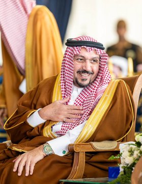 مجموعة من الرجال في الزي التقليدي السعودي يجلسون في قاعة مزخرفة بألوان زرقاء وذهبية مع ستائر وكراسي فاخرة وطاولات تحمل باقات من الزهور البيضاء، بعضهم يصفقون، ويظهر رجل في الزي العسكري بينهم، الإعداد يشمل مكبر صوت وديكورات رسمية. رجل في ثوب بني مع غترة حمراء يجلس مبتسمًا ويضع يده على قلبه في كرسي خشبي مزخرف مع باقة زهور بجانبه. رجل في ثوب أبيض مع غترة سوداء يقف خلف منصة ويتحدث في ميكروفون مع نظارات وأوراق في يده في قاعة رمادية. رجل في ثوب أبيض مع غترة حمراء يقف خلف منصة بيضاء تحمل شعارًا يظهر جملًا ونصًا عربيًا ويتحدث في ميكروفون مع رجال في الخلفية.