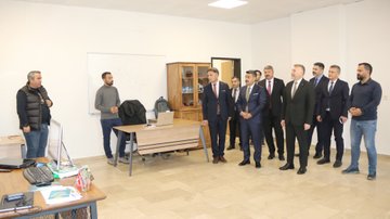 First image shows eight men in suits and casual attire standing in a modern office entrance with MEBİ logo on the wall and a large blue robot mascot figure waving nearby. Second image depicts over ten men in formal suits gathered around a desk and whiteboard in a classroom-like room with wooden cabinets and a projector screen. Third image features five men, one gesturing while standing near desks with laptops, monitors, and office chairs in a workspace. Fourth image displays nine men in mixed attire including suits and sweaters positioned around desks in an open office area with electrical outlets visible.