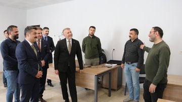 First image shows eight men in suits and casual attire standing in a modern office entrance with MEBİ logo on the wall and a large blue robot mascot figure waving nearby. Second image depicts over ten men in formal suits gathered around a desk and whiteboard in a classroom-like room with wooden cabinets and a projector screen. Third image features five men, one gesturing while standing near desks with laptops, monitors, and office chairs in a workspace. Fourth image displays nine men in mixed attire including suits and sweaters positioned around desks in an open office area with electrical outlets visible.