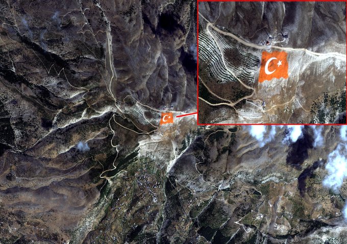 Satellite view of rugged mountainous terrain in Kahramanmaraş with snow-covered peaks and valleys. Red outlined area highlights a striped pattern resembling the Turkish flag body on the slope near Ahır Dağı summit. Orange Turkish flag emblem with white crescent and star is placed at the top center of the design. Red arrow points to a small structure or marker on the ground below the flag. Overall composition shows the flag formation integrated into the natural landscape from space.