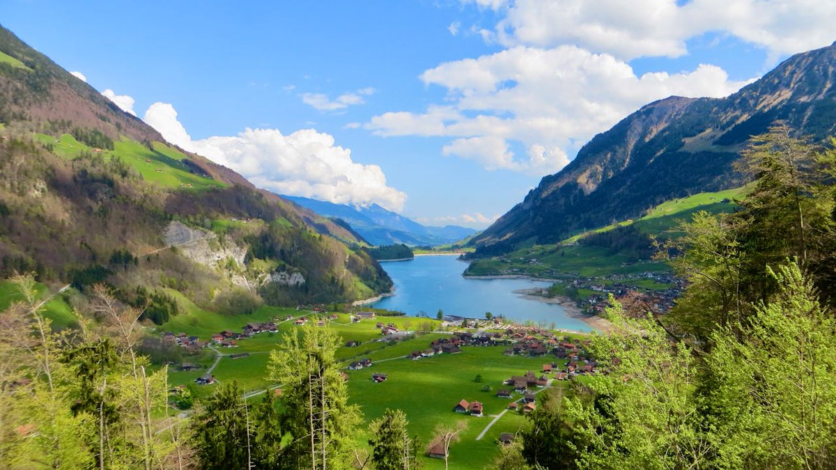 CommSnap's tweet image. This royalty-free photo captures Lungern in Switzerland, showcasing in alpine valley surrounded by steep mountain slopes and scattered village houses. The layout leads the viewer’s eye through the valley towards the lake and distant peaks, illustrating harmony between nature and…