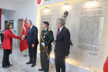 Multiple images depict formal handshakes during a ceremony in a room with Turkish flags and a wall featuring Turkish commemorative text and silhouette. Dignitaries including men in suits and military uniforms with medals and swords exchange greetings. A woman in red attire participates in one handshake. The setting includes decorative lighting and official plaques.