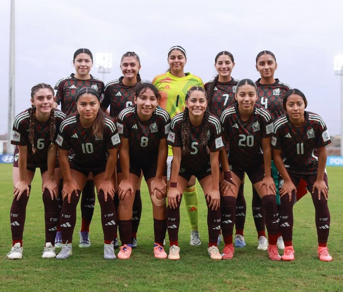 Group of eleven young women soccer players from the Mexican national team posing together on a green soccer field under stadium lights, wearing matching green jerseys with numbers like 6, 10, 5, 7, 4, 11, and the team emblem, black shorts, knee-high socks, and cleats in white and green, with the goalkeeper in a yellow jersey, all smiling and kneeling or standing in formation.