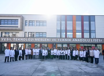 First image shows a man in a suit and keffiyeh smiling and hugging a group of young students in green shirts with school logos, standing in front of a banner reading Bir Okul Bin Umut Gazze, under trees in an outdoor school setting. Second image depicts the same man in suit and keffiyeh interacting with a diverse group of adults and youth near a food stand with trays of pastries, cookies, and dishes on a table, outdoors with autumn foliage and a metal shelter. Third image features the man in suit and keffiyeh standing with students in green shirts beside a trophy on a table inside a building with Turkish flag, a red box, and award plaques visible. Fourth image displays a large group of people in white lab coats and suits posing in front of the Yesil Teknoloji Mesleki ve Teknik Anadolu Lisesi building entrance on a sunny day.