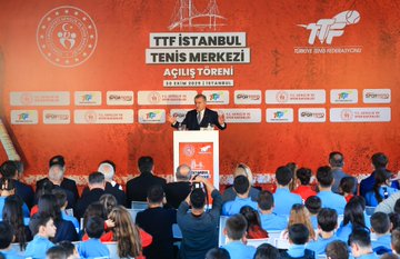 First image shows a man in a suit standing at a podium speaking with a microphone in front of a large red banner displaying TTF Istanbul Tenis Merkezi logo and Turkish Tennis Federation branding surrounded by sponsors like Spor Toto and attendees seated in blue uniforms. Second image captures a group ribbon-cutting ceremony with officials including men and women in formal attire and children in red and blue tracksuits smiling and holding scissors in front of a similar red banner with tennis racket graphics. Third image features a close-up of the minister in a suit embracing and interacting with children in blue uniforms near a tennis net setup against the branded backdrop. Fourth image is an aerial view of the tennis facility with multiple red clay courts stands lighting poles surrounding greenery an indoor dome structure and nearby urban buildings with sea in the background.
