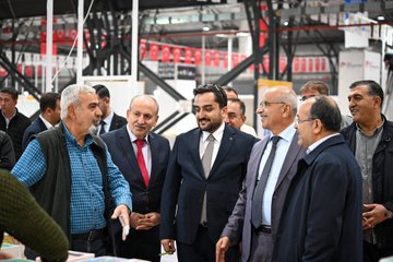First image shows a man in a blue shirt shaking hands with a man in a gray suit and tie in front of book stacks and fair booths with Turkish flags and banners including Malatya Ticaret Borsası. Second image depicts a group of men in suits and casual attire gathered around discussing near book displays and exhibition stands with Turkish flags in a large indoor fair hall. Third image features men in formal wear including suits and vests shaking hands and standing near book stalls with promotional posters and Turkish flags at the event. Fourth image displays several men in suits standing together in front of stacked red and white books and fair booths labeled with numbers and Malatya Ticaret Borsası in a spacious exhibition area.