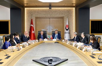 First image shows two men in suits standing at podiums holding blue and red folders with logos one with glasses wearing a blue tie and the other in a blue suit with a blue tie Turkish and Italian flags on either side wooden doors in background. Second image depicts a long conference table with multiple suited men and women seated around it including bald man and woman with glasses Turkish and Italian flags and TÜBİTAK logo on walls modern room with lighting. Third image features a group of eight suited men and women standing in front of large screens displaying Turkish Italian and another flag wooden table with microphones below. Fourth image shows five people seated around an oval table in suits including bald man and woman with headscarf Turkish Italian and other flags in background conference setup with documents.
