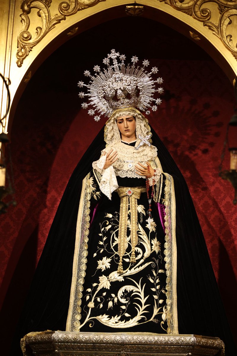 HdadHiniesta's tweet photo. 🖤 LA VIRGEN DE LA HINIESTA DOLOROSA EN EL MES DE LOS DIFUNTOS |

En este mes de los fieles difuntos, la Santísima Virgen de la Hiniesta Dolorosa viste su tradicional atuendo de luto, símbolo de oración y recuerdo por quienes ya gozan del descanso eterno.

Luce saya y manto de terciopelo negro. La saya, con apliques en oro con motivos florales y vegetales, fue realizada por NHD Joaquín Sánchez Blanco y NHD José María García Rodríguez en 1996. Ese mismo año, NHDoña Lorena Montero Rodríguez donó el manto, de terciopelo liso con galón dorado y forro morado. Sobre sus sienes, corona de metal plateado utilizada para su bendición en 1937. 

También luce broche relicario de Santa Ángela de la Cruz de plata sobredorada donado por un grupo de hermanos, broche de plata y nácar con relicario de María Santísima de la Hiniesta desaparecida en 1932 donado por NHD José Maria Ruiz Rueda, tocado de encaje duquesa estrenado en 2024 y donado por el grupo de priostía, broche con su nombre en plata y puñal de plata donado por NHD Emilio Balbuena Arriola en sus bodas de plata como hermano de la corporación. 
Como estreno, destacamos el rosario de ambar natural facetado y filigrana de plata del siglo XVIII donado por la familia Martín Jaén.

🕯️ Santísima Virgen de la Hiniesta Dolorosa, ruega por todos los fieles difuntos.

#SoydeLaHiniesta
#LaEstrellaSublime