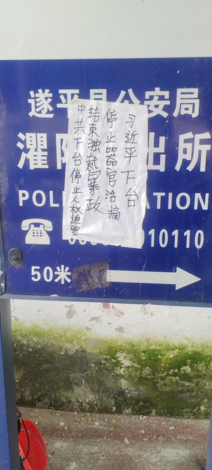 First image shows a blue police station signboard with Chinese text including 报警 and 110 emergency number, a white paper notice pasted over it with handwritten Chinese characters protesting against CCP and calling for freedom, and a red phone attached to the wall. Second image displays a beige wall with a large white paper poster covered in dense handwritten Chinese text denouncing CCP tyranny, human rights abuses, and demanding release of political prisoners like Feng Yongjun. Third image features a red wall with a smaller white paper strip containing handwritten Chinese text criticizing CCP dictatorship and advocating for democracy and freedom. Fourth image depicts a white utility pole on a street with parked vehicles and scooters in the background, graffiti in black Chinese characters reading 法轮大法好真善忍 meaning Falun Dafa is good, truthfulness compassion forbearance.