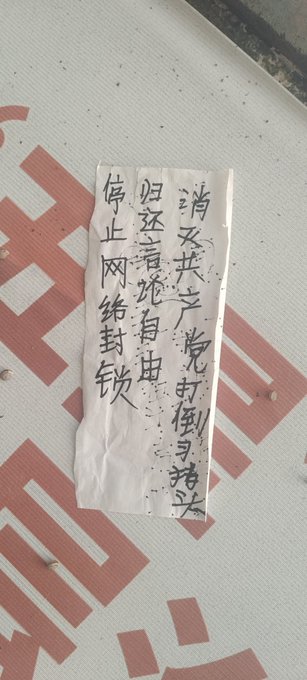 First image shows a blue police station signboard with Chinese text including 报警 and 110 emergency number, a white paper notice pasted over it with handwritten Chinese characters protesting against CCP and calling for freedom, and a red phone attached to the wall. Second image displays a beige wall with a large white paper poster covered in dense handwritten Chinese text denouncing CCP tyranny, human rights abuses, and demanding release of political prisoners like Feng Yongjun. Third image features a red wall with a smaller white paper strip containing handwritten Chinese text criticizing CCP dictatorship and advocating for democracy and freedom. Fourth image depicts a white utility pole on a street with parked vehicles and scooters in the background, graffiti in black Chinese characters reading 法轮大法好真善忍 meaning Falun Dafa is good, truthfulness compassion forbearance.