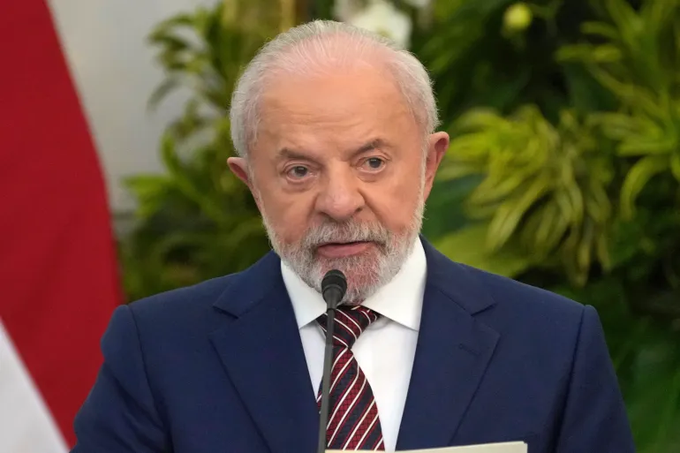 First image shows an elderly man with white hair and beard wearing a blue suit red tie and white shirt speaking into a microphone at a podium with green plants and a red flag with yellow diamond in background. Second image shows a man with gray hair and mustache wearing a yellow jacket with blue stars raising his right fist in a gesture with blurred crowd and red background with white text possibly a stage setting.