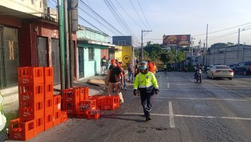 Multiple images depict a street scene in an urban area with colorful buildings and power lines. Orange plastic crates from a spilled truck load are stacked on the road near a pole. People in high-visibility yellow vests, including police officers, stand around directing traffic and assisting with cleanup. Motorcycles and cars are visible on the wet pavement. A Coca-Cola truck and a building with Elephant sign appear in some frames. Traffic cones and a fire truck are present in one image.
