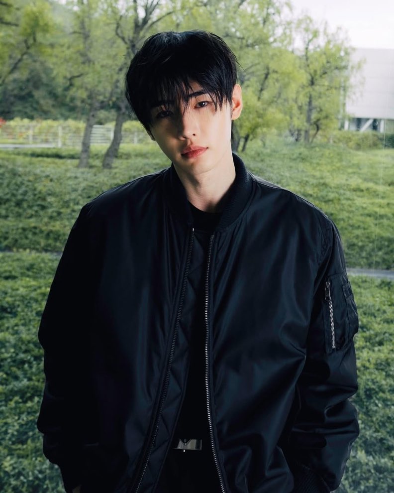 Sunghoon radiates a striking elegance in this Prada shoot, his sleek black jacket blending with lush greenery, exuding timeless sophistication and commanding allure against Tuscany’s serene backdrop.