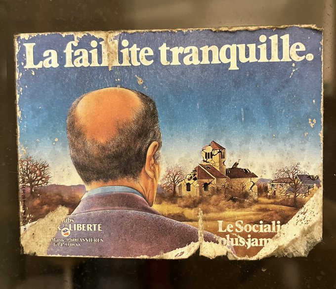 Vintage poster illustration shows a bald man in a dark suit viewed from behind standing in a rural setting with barren trees a stone church on a hill and distant landscape under a blue sky. Prominent text overlay reads La fausse tranquillite du socialisme plus jamais in bold letters with Le Socialisme at the bottom and LIBERTE in the lower right corner.