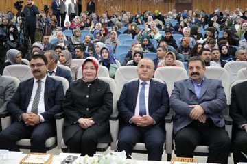 First image shows rows of attendees in formal attire seated in an auditorium with wooden walls Turkish flags and a table with flowers at the front. Second image depicts a woman in headscarf speaking at a podium with microphones and a university logo on the stand against a dark curtain backdrop. Third image features a man in suit at a podium with microphones in front of a screen displaying event title Calisma Yurdunda Din Ogrenimi Vizyonu Turkiye 31 Ekim-17:00 Saat 09:00-17:00 and logos. Fourth image displays a group of officials including men in suits and women in headscarves seated on stage with microphones and flowers in front of an audience.