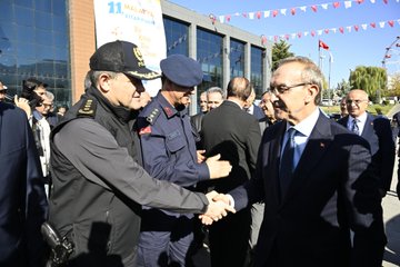 First image shows a man in black jacket and cap shaking hands with a man in suit against a building with Turkish flags and Malatya banner. Second image depicts rows of seated people in suits and traditional attire in a red-carpeted auditorium with Turkish flags, flowers, and book fair banners. Third image captures a man in suit speaking at a white podium with microphones in front of a large banner for 11. Malatya Anadolu Book Fair, including guitars and chairs nearby. Fourth image features police officers and civilians in uniforms and casual clothes at an exhibition stand with Turkish flags, informational banners about police services, and a table.