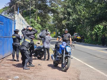Multiple images depict uniformed police officers in tactical gear standing near motorcycles and vehicles on a rural road with graffiti-covered walls trees and a blue container in the background. Officers are positioned around parked motorcycles and cars suggesting a checkpoint or patrol. Another image shows officers near a blue container and motorcycles on a road with lush greenery and a sign. A third image features a motorcycle parked near a gated entrance with yellow trees potted plants and vehicles in a compound-like area. The final image shows the entrance to Cementerio General Taxisco Santa Rosa with a yellow building arched gate police officers on motorcycles and civilians including people in casual clothing near umbrellas and tables under sunny conditions.