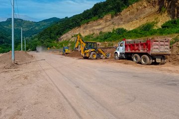 First image shows a yellow excavator digging dirt near a white dump truck loaded with red soil on a roadside with mountainous terrain, green hills, and utility poles in the background. Second image depicts a close-up of a yellow excavator with extended arm and bucket positioned on dirt ground beside a pile of soil, surrounded by lush green vegetation and a road. Third image features two yellow excavators, one scooping soil into a red dump truck on a dirt road with sloped hills and scattered dirt mounds. Fourth image displays a red and beige surveying instrument on a tripod with a digital screen, set up on dirt ground overlooking green forested hills under a blue sky, with a person standing nearby.