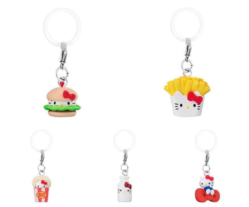 Five clear plastic keychain accessories shaped as American fast food items with Hello Kitty character integrated: a pink burger with Hello Kitty face on bun, yellow fries container topped with Hello Kitty head, white milk bottle featuring Hello Kitty on label, red popcorn bucket with Hello Kitty sitting on top, and a heart-shaped element attached to one.