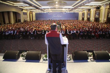 First image shows a man in a red and white vest standing at a blue podium pointing emphatically during a speech, with a large blue banner behind reading 20 Turkıyeye Buluşması 1 Kasım 2025 Antalya and Memur-Sen logo. Second image depicts a large audience of people in formal attire seated in rows on a carpeted floor in a grand hall with blue banners reading Sendika and floral decorations. Third image captures another crowded conference room with attendees in suits and dresses seated under chandeliers and blue banners reading Sendika. Fourth image features the same man from behind at a podium addressing a vast seated audience in a spacious hall with blue Sendika banners and floral arrangements.