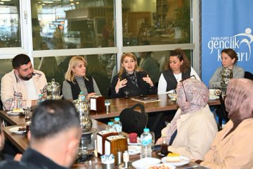 First image shows a large group of adults and children posing in front of a building entrance with a green sign reading Barguzu Sosyal Tesis, some holding a baby, all dressed in casual and formal winter clothing. Second image depicts four women seated at a wooden table with plates of food, glasses of water, and desserts, one child in a pink hat sitting among them, background showing windows and blurred people. Third image features a group of men and women around a table with food items like pastries and drinks, a blue banner with Turkish text for youth center, some wearing headscarves, gesturing during discussion. Fourth image captures another group of adults and a woman holding a baby outside a building entrance with plants and lights, all in coats and jackets.