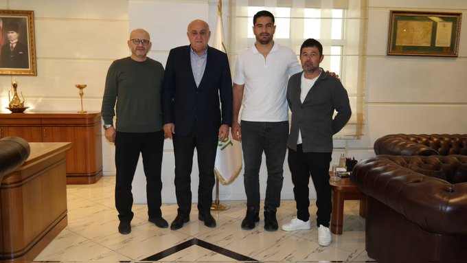 First image shows two men standing in an office: one in a blue suit holding a green flag, the other in a white polo shirt and dark pants, with Turkish flag on a stand, wooden desk, leather sofas, framed portrait on wall, vase and candlestick on side table. Second image shows four men standing together in similar office: leftmost in green sweater and dark pants, next in blue suit with green flag, third in white polo shirt and dark pants, rightmost in gray vest and white sneakers, same background elements including flag, desk, sofas, portrait, vase.